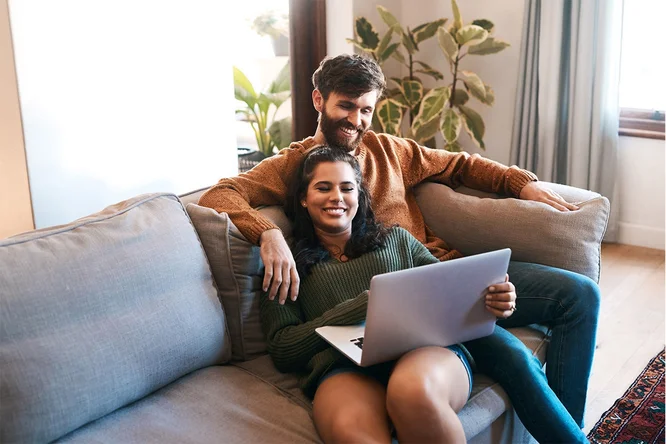 Mladi par opušteno sjedi na kauču i gledaju u laptop