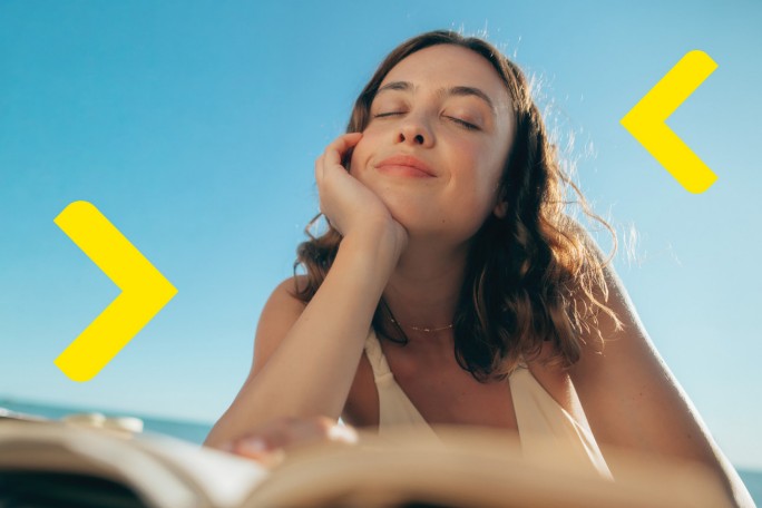 Smiling happy young woman giving her friend a lift in her car in town, profile view through the open side window with sun flare