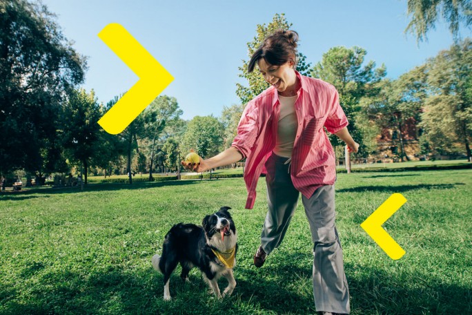  RBI ChatGPT now A person is lying on a blanket on the grass, holding a smartphone and looking at the screen. Next to the person, on the blanket, is a dog. Nearby, there is an open book and a yellow rubber dog bone.